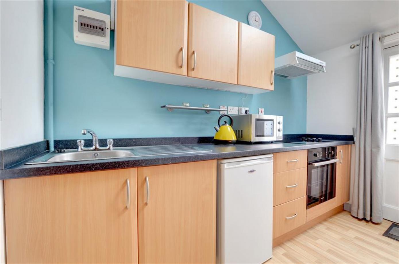 The fully equipped kitchen in one of the Cranbrook holiday lets, showing an oven, a microwave, a fridge a sink and cupboards for accomodation in Kent..