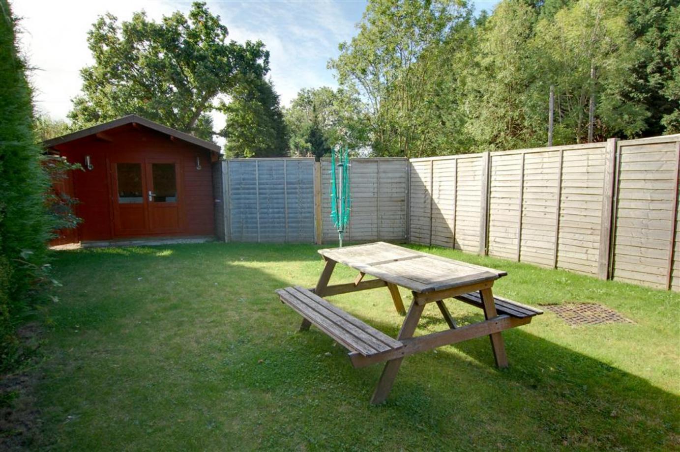 The shared enclosed garden in the Cranbrook holiday lets, showing a patch of grass with the out house and a table and benches and a washing line for accomodation in Kent..